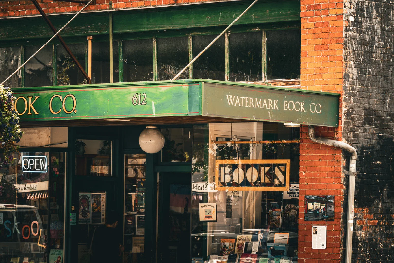 A quaint bookstore named Watermark Book Co. with a green awning and a hanging BOOKS sign is located on a brick building.