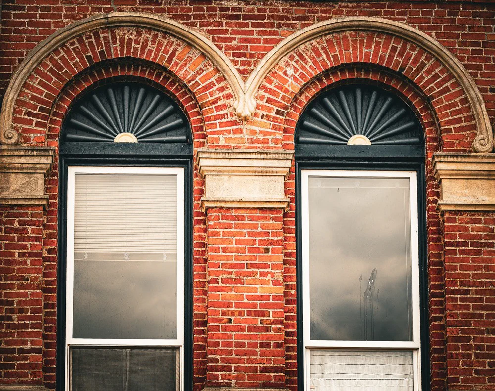 Two arched windows with decorative fan-shaped transoms are set in a red brick wall.