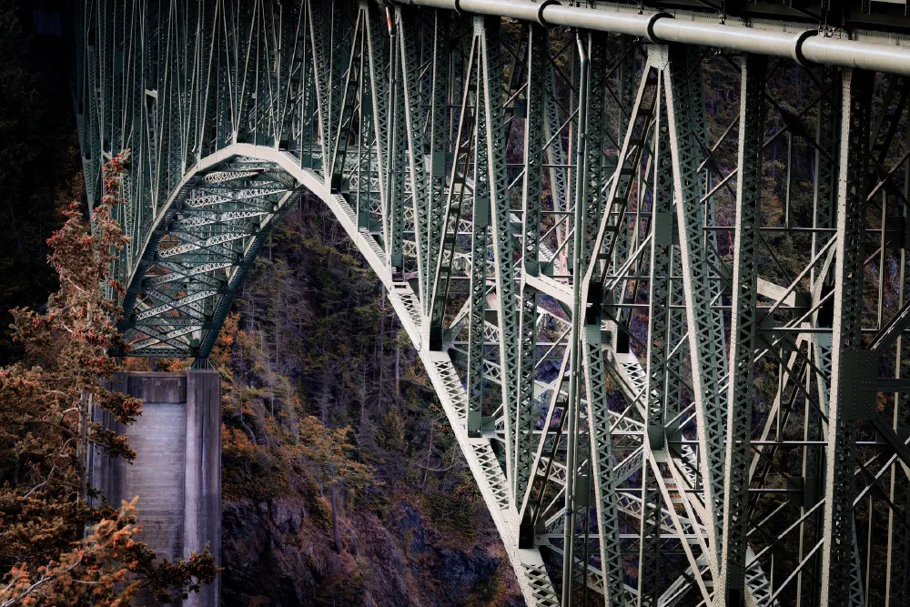 A large steel arch bridge spans a deep canyon surrounded by trees and rocky cliffs.