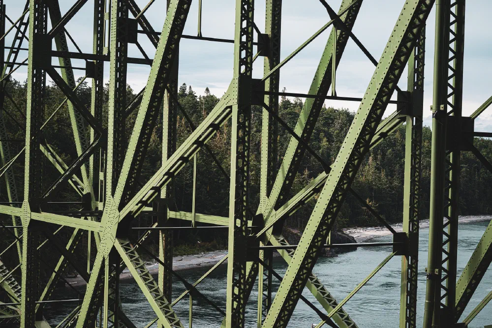 A green metal truss bridge spans over a river with trees visible in the background.