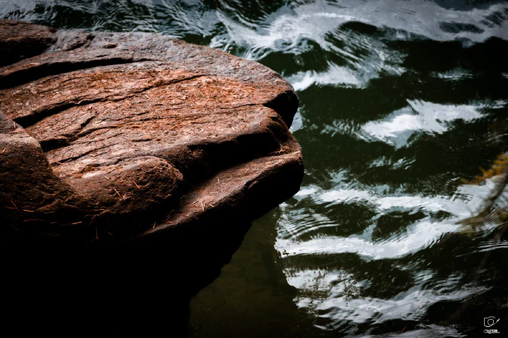 A textured reddish-brown rock extends over dark, rippling water.