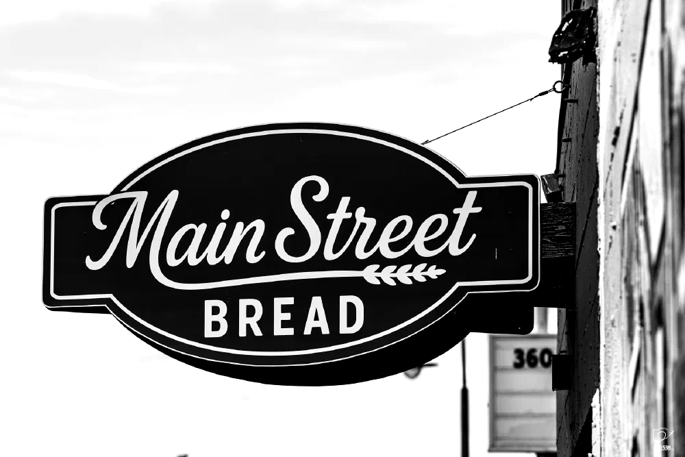 A black and white sign for Main Street Bread is mounted on the side of a building.