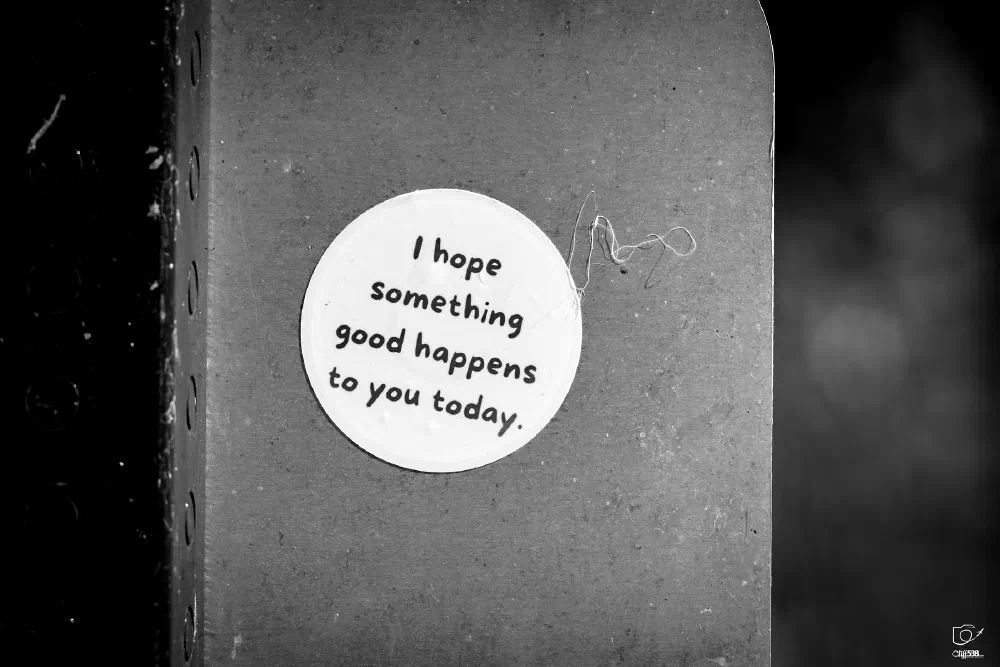 A round sticker with the message I hope something good happens to you today is attached to a textured surface.