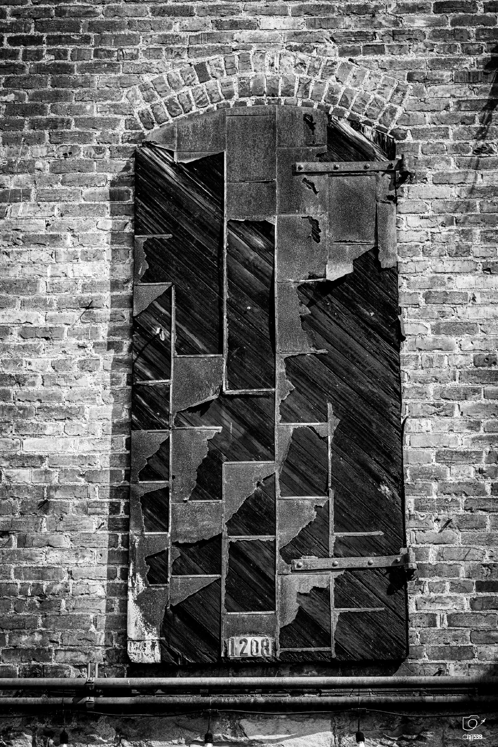 A worn, patchwork wooden door with peeling paint is set within an arched brick wall.