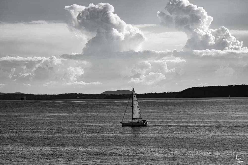 A lone sailboat glides across calm waters under a sky filled with large, dramatic clouds.