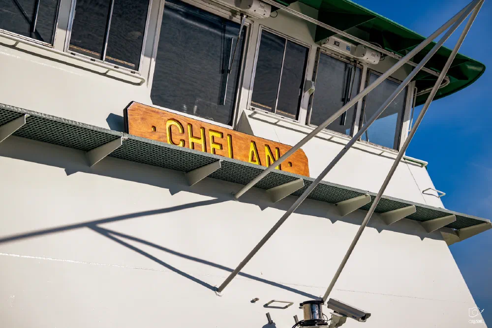 The side of a white boat named Chelan is shown with windows and metal beams extending outward.