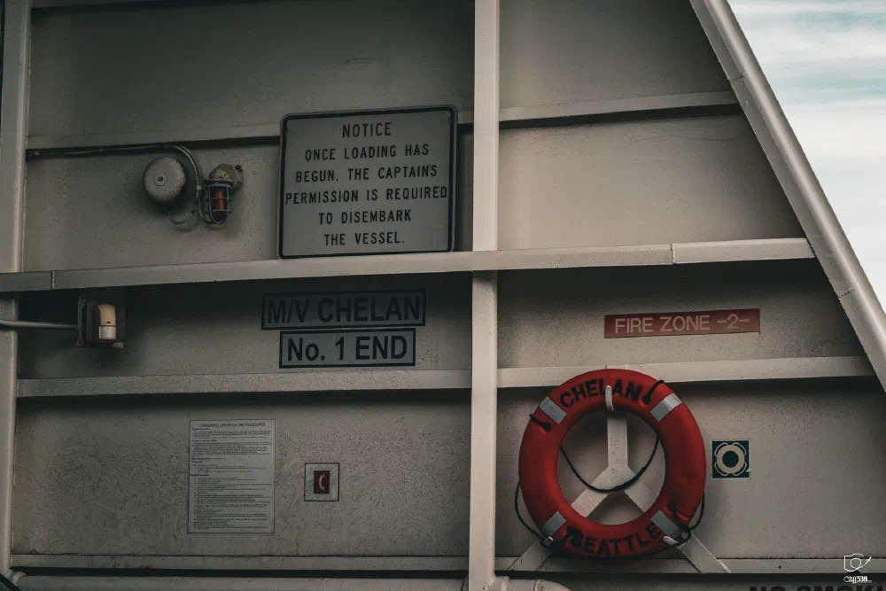A section of a vessel named MV Chelan displays safety signs, a life preserver, and instructions regarding permission needed to disembark.