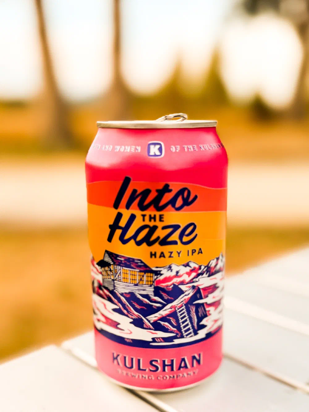 A can of Into the Haze Hazy IPA beer from Kulshan Brewing Company is placed on a white surface with a blurred outdoor background.