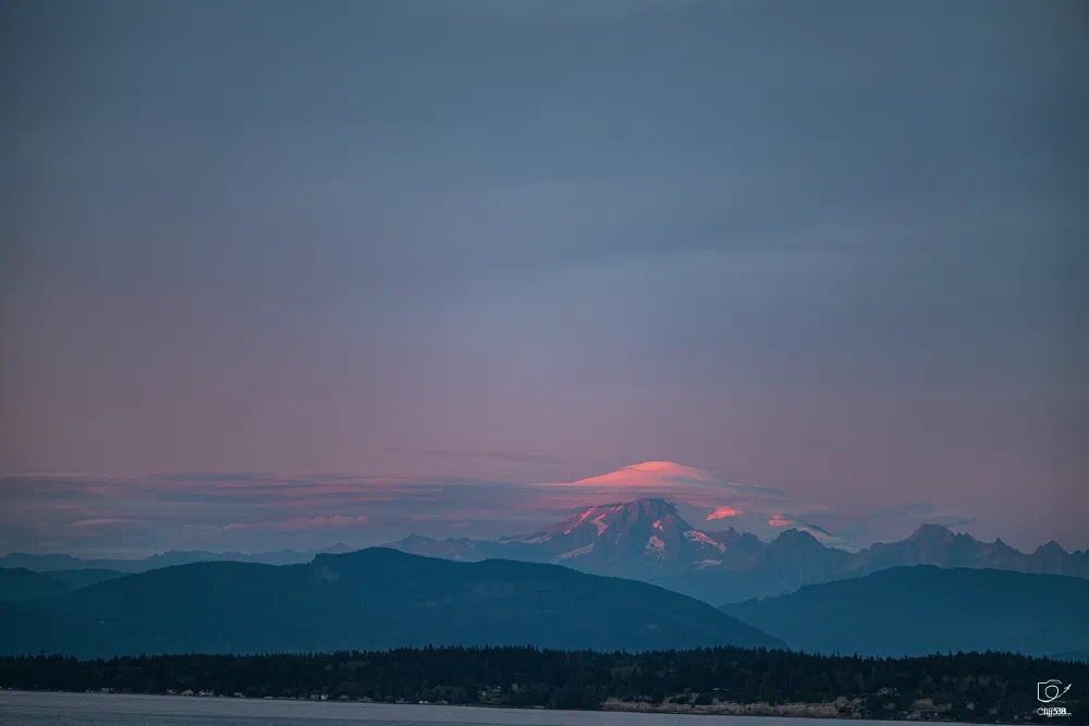 A serene landscape features distant mountains illuminated by soft pink and purple hues under a calm sky.