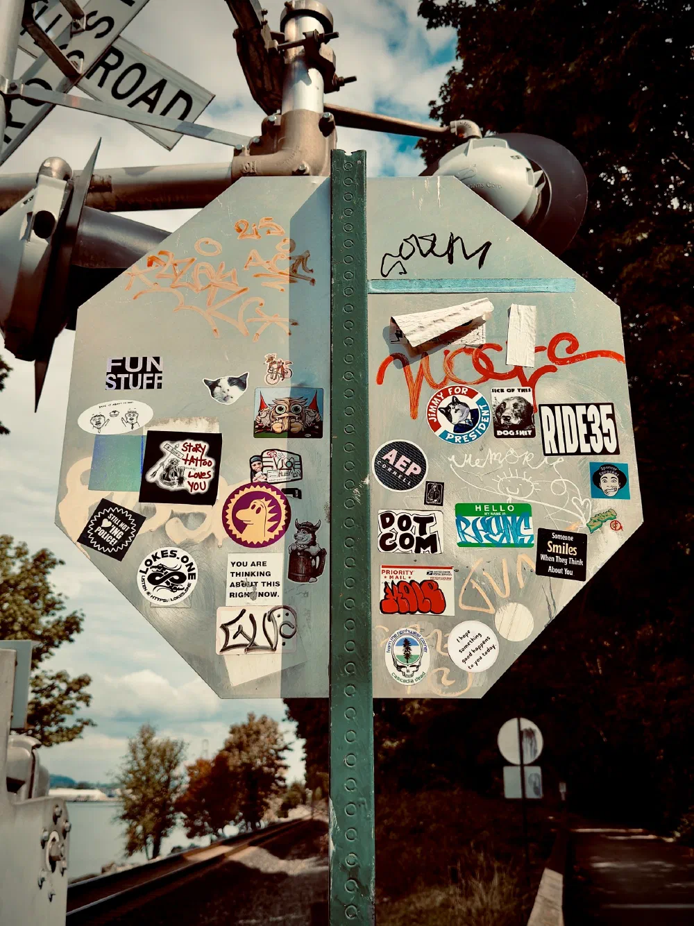 A railroad crossing sign is covered with various colorful stickers and graffiti.