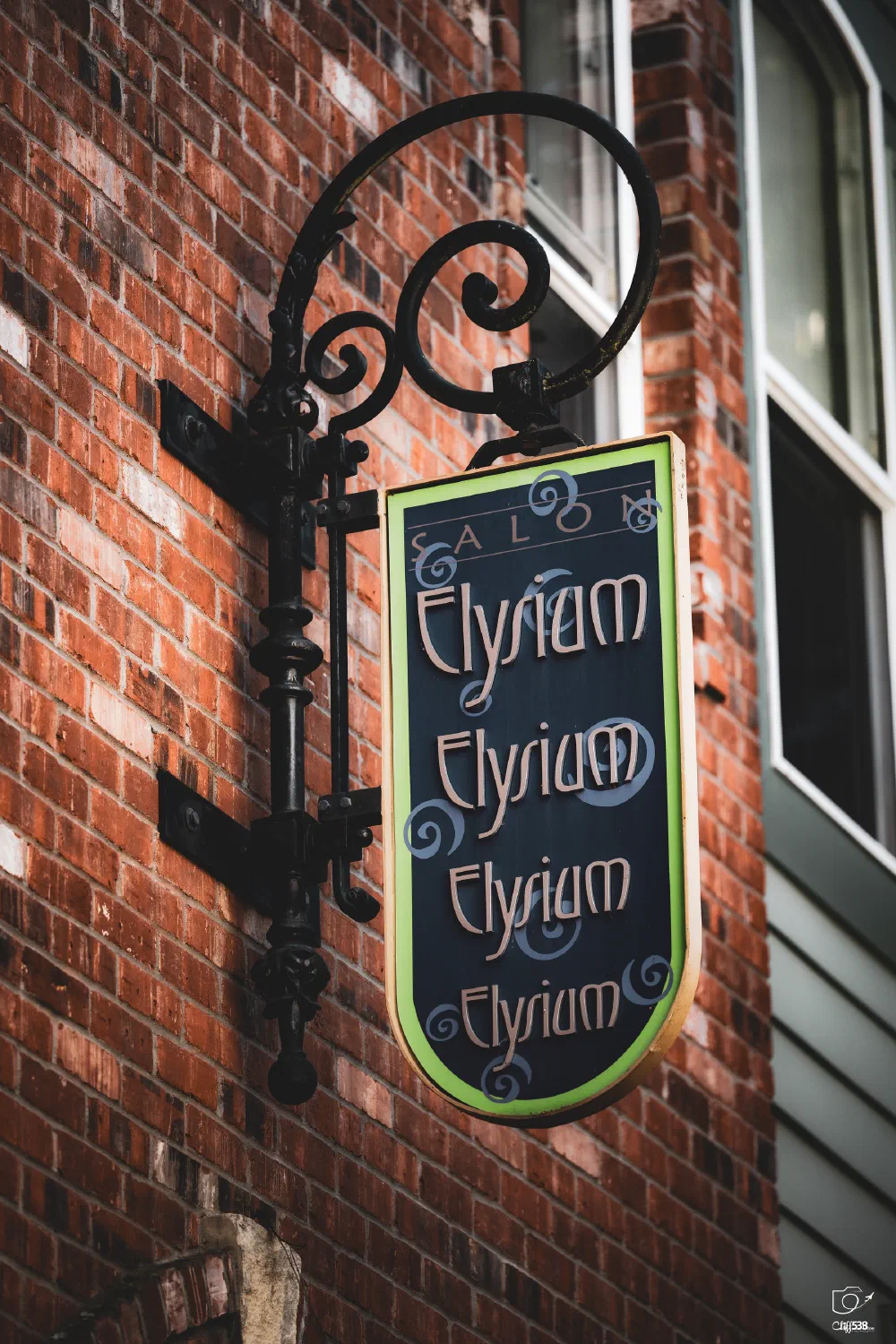 A decorative hanging sign with the word Elysium repeated multiple times is mounted on a brick wall next to a window.