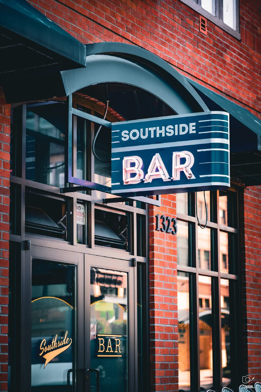 A blue and white sign reading Southside Bar hangs above the entrance of a brick building with the address number 1323.