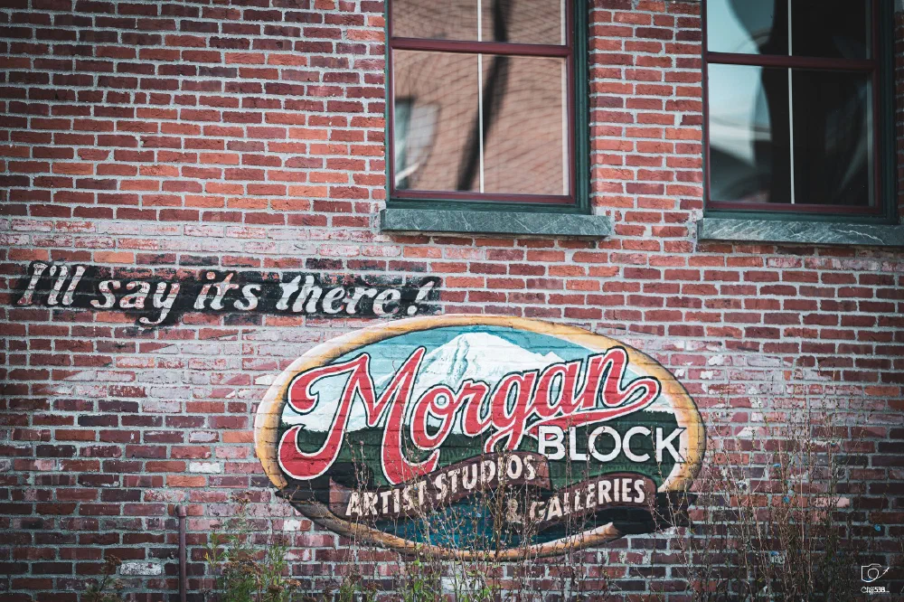 A painted sign on a brick wall reads Morgan Block Artist Studios Galleries alongside the phrase I'll say it's there! in a cursive font.