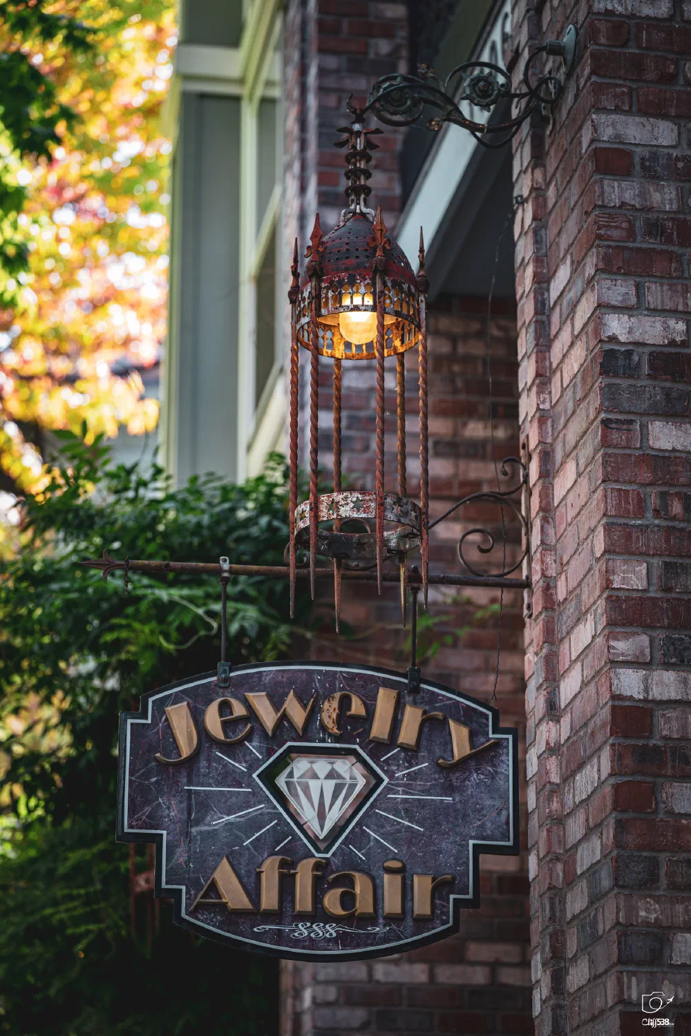 A decorative lantern hangs above a sign for a jewelry store named Jewelry Affair attached to a brick wall.