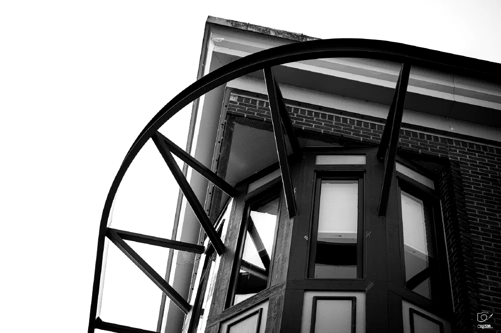 A close-up view of a building corner features large windows and a geometric metal structure arching above.