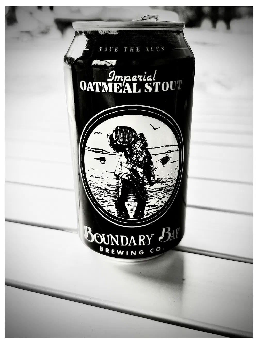 A black can of Boundary Bay Brewing Co.'s Imperial Oatmeal Stout with a vintage-style illustration of a man carrying a keg is placed on a white surface.