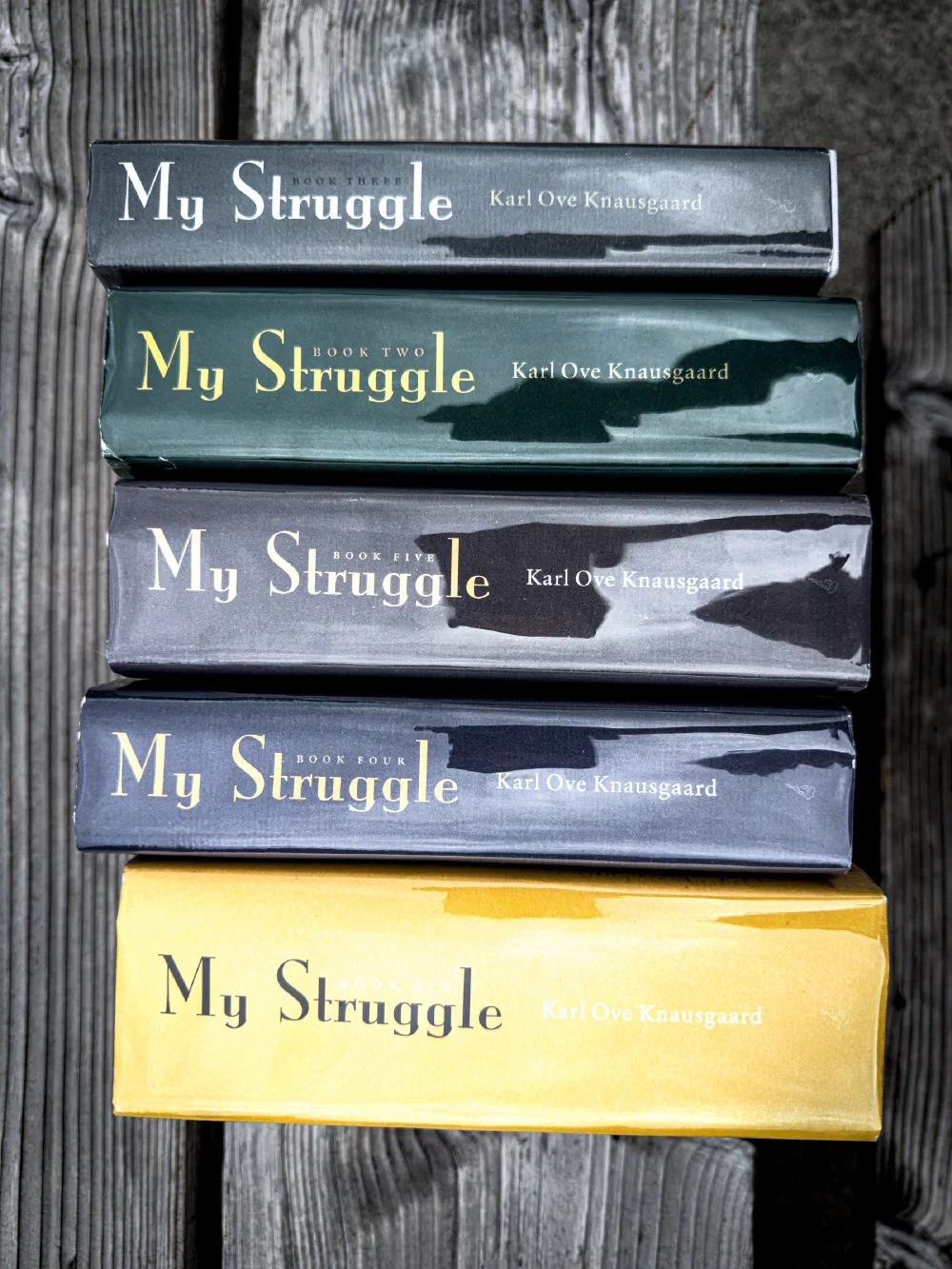 A collection of five hardcover books titled My Struggle by Karl Ove Knausgaard is stacked on a wooden surface.