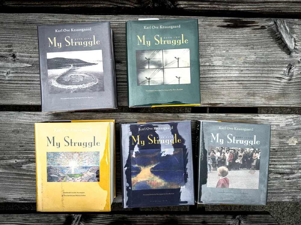 Five volumes of Karl Ove Knausgaard's book series My Struggle are arranged on a wooden surface.