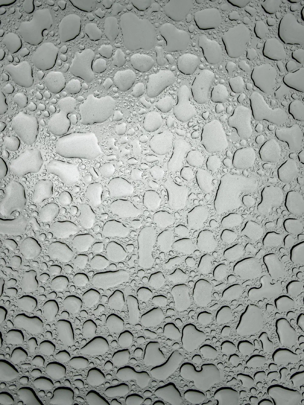 Water droplets of various sizes are scattered across a smooth, transparent surface, creating a pattern of reflections and refractions.
