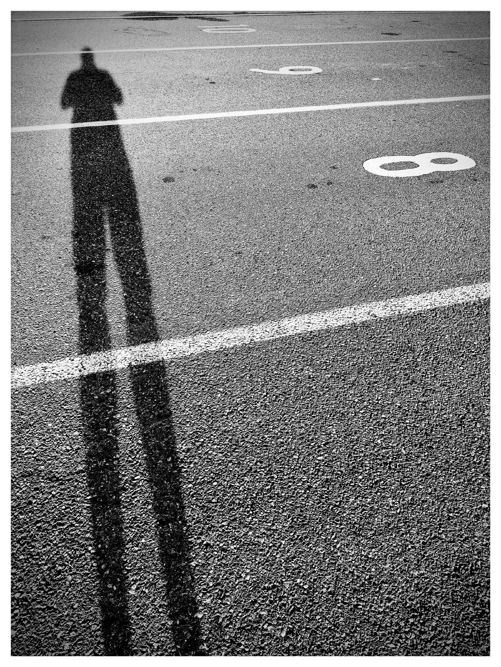 A long shadow of a person is cast on a numbered parking lot pavement.