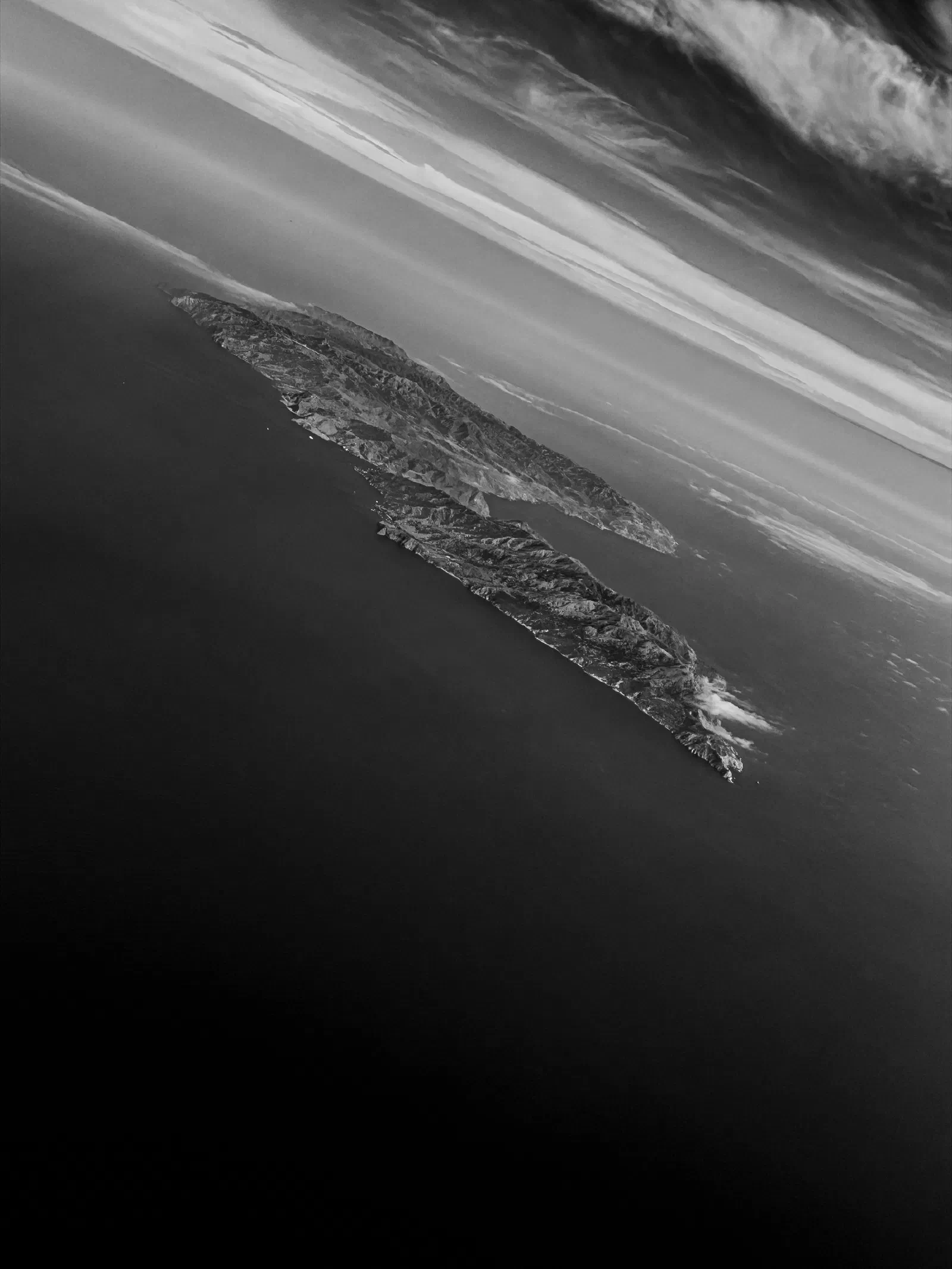 A rocky island is surrounded by the ocean under a dramatic sky with layered clouds.